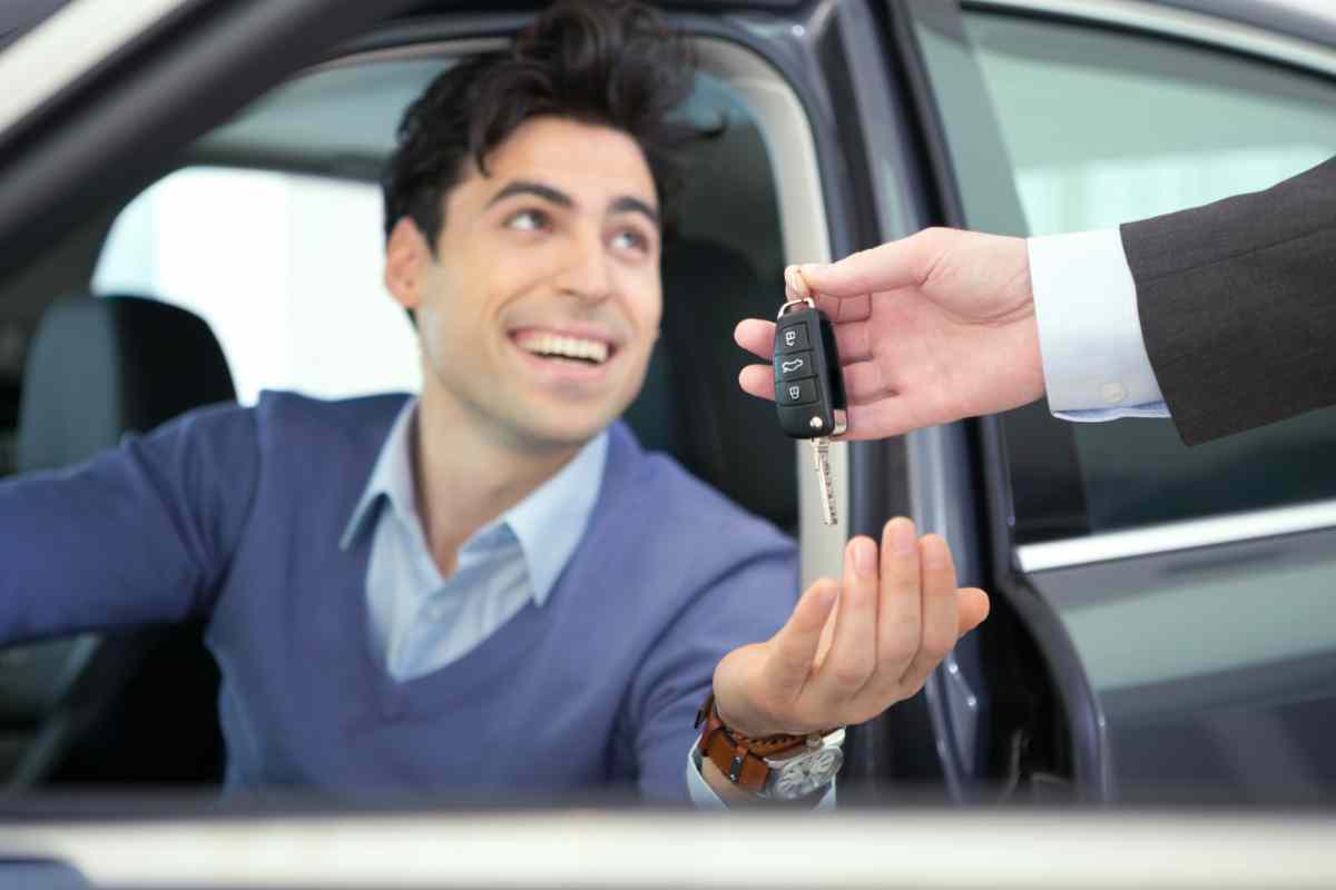uomo seduto al volante prende le chiavi dell'auto dal concessionario